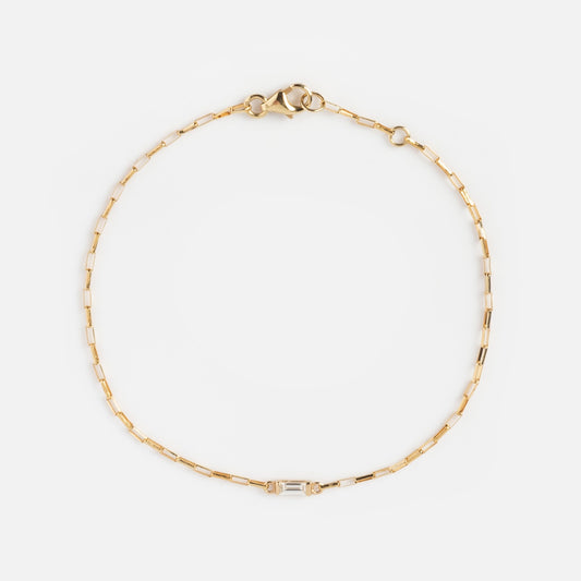 The Sunblink Diamond Bracelet is a delicate gold chain with rectangular links, featuring a small baguette-cut clear stone at the center and secured by a lobster clasp.
