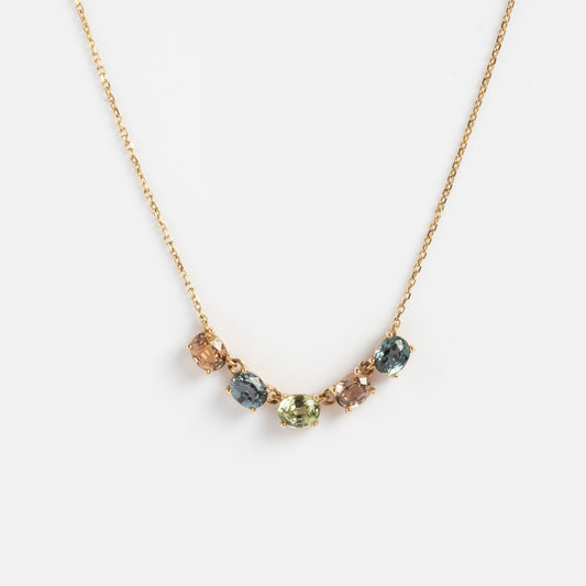 The Royal Mile Necklace is a delicate gold chain featuring five cushion-cut gemstones—light brown, blue, and light green—elegantly curved at the center.