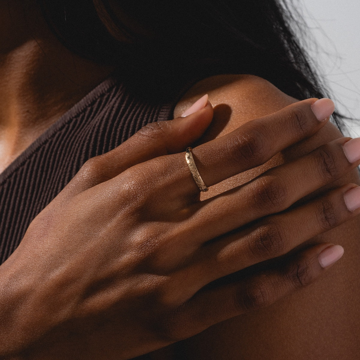 A close-up of a hand resting on a shoulder showcases the Dukes Champagne Diamond Ring on the finger. The wearer pairs it with a sleeveless, ribbed brown top and has neatly manicured, natural nails.