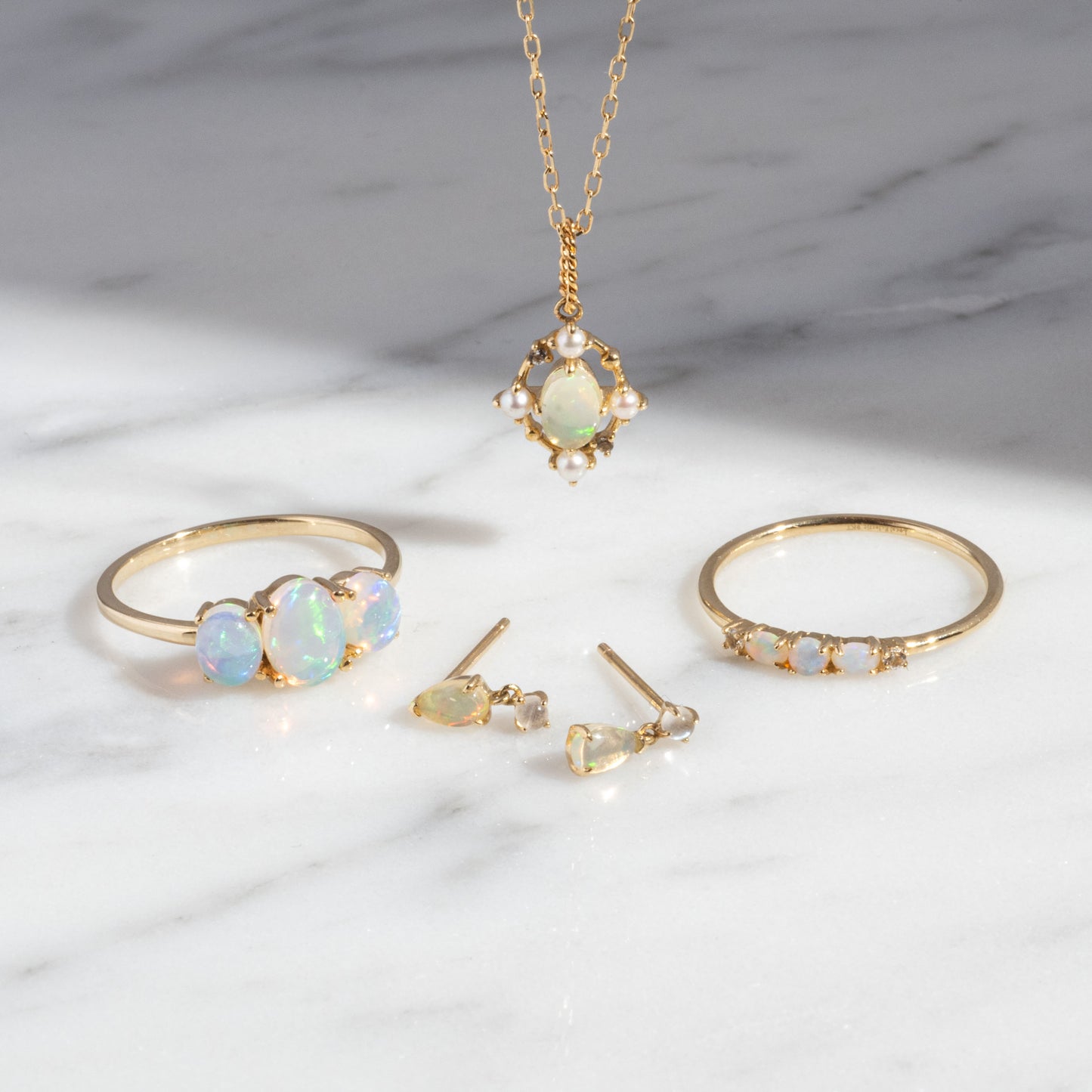 The Solid Gold 2025 October Capsule Opal Ring Set is shown on marble, featuring a ring, necklace, earrings, and bracelet with iridescent opals and pearl accents—includes a free gift.