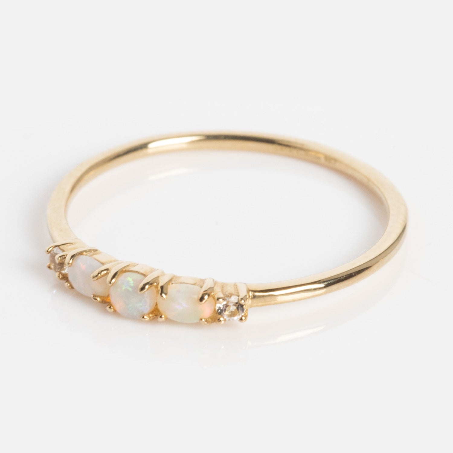 The Solid Gold 2025 October Capsule Classic Opal Trio Statement Ring showcases three oval opals and two clear gemstones set in a row on a slim gold band, displayed on a plain white background.