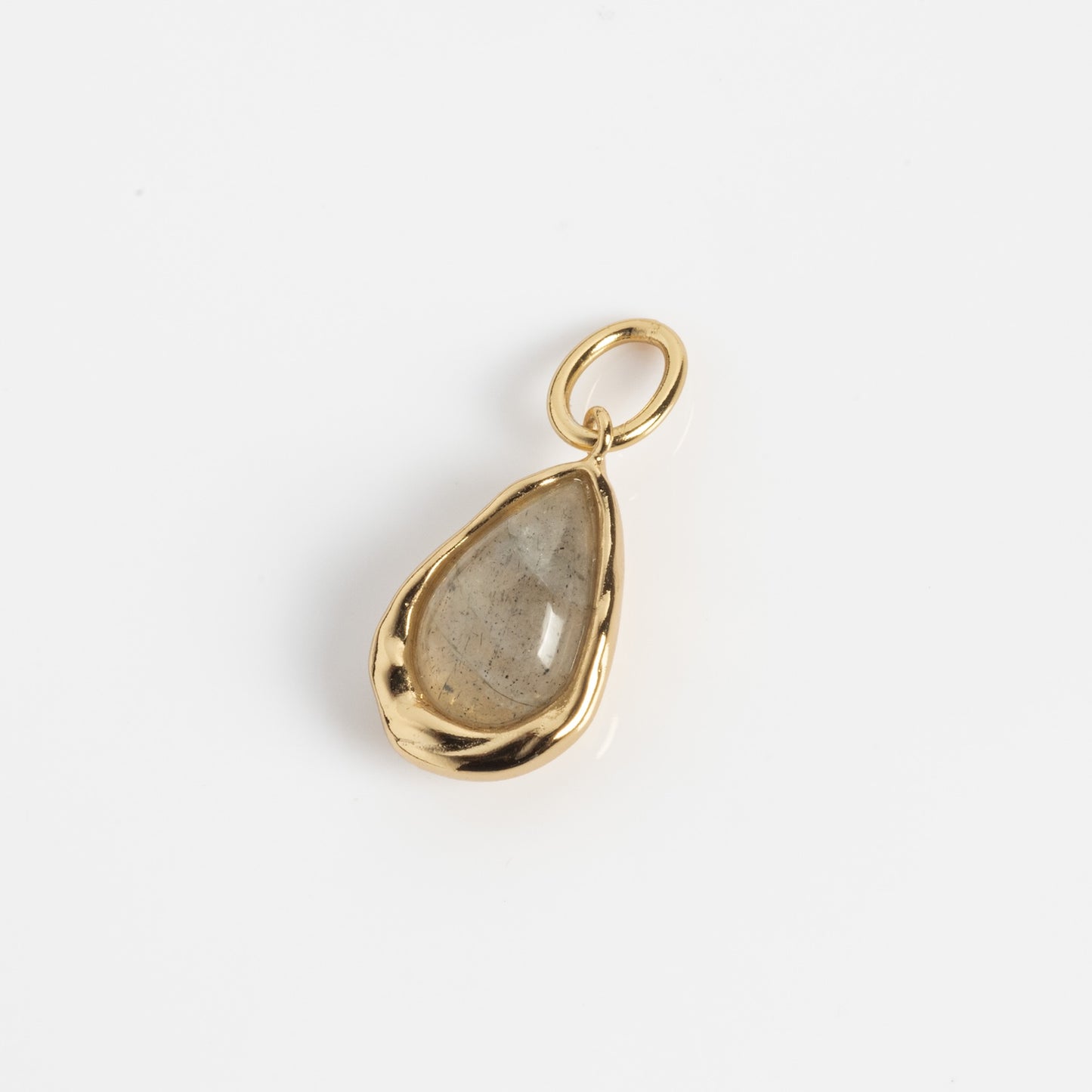 The Labradorite Charm Sample features a teardrop-shaped translucent labradorite pendant with natural inclusions, set in a yellow gold-plated brass bezel and loop, shown on a white background.