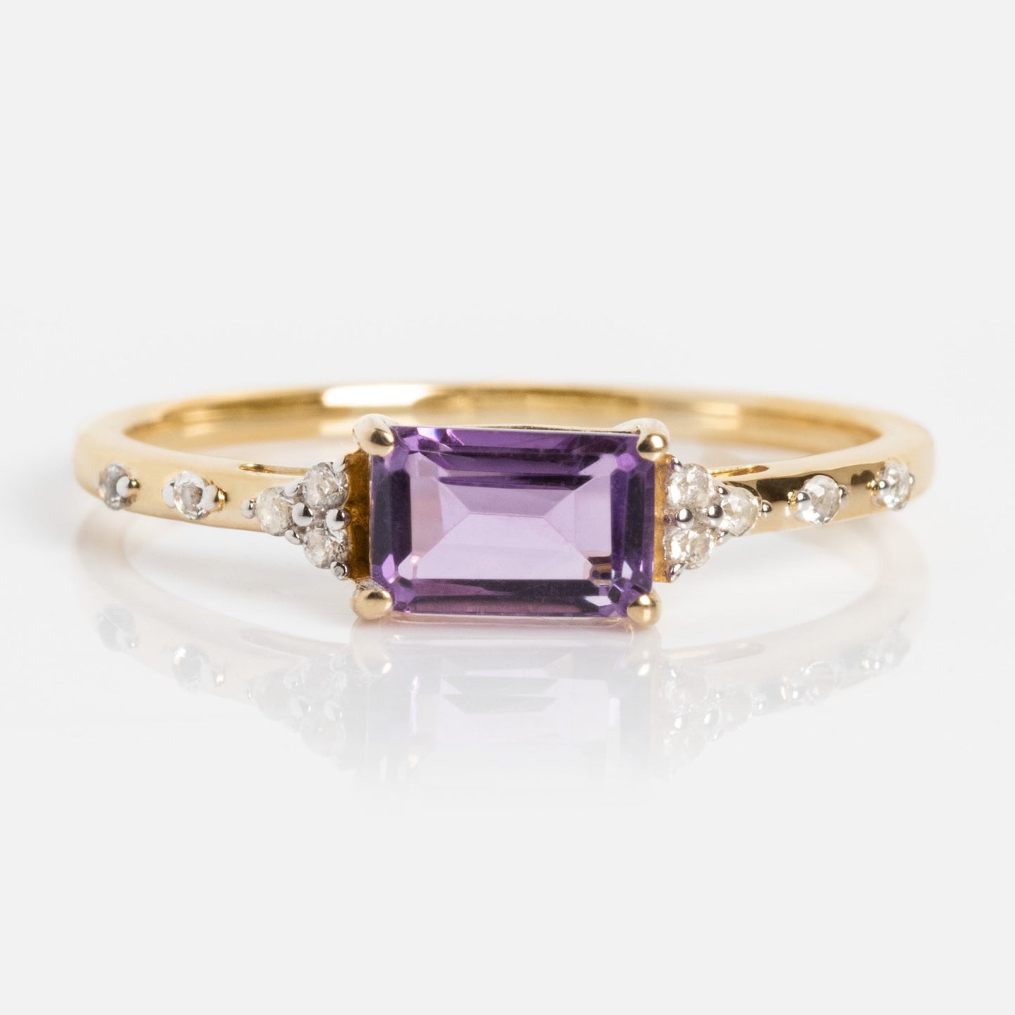 The Solid Gold Glimmering Birthstone Baguette Ring showcases a rectangular purple gemstone at the center, accented by round diamonds along the band, and is displayed on a white background.