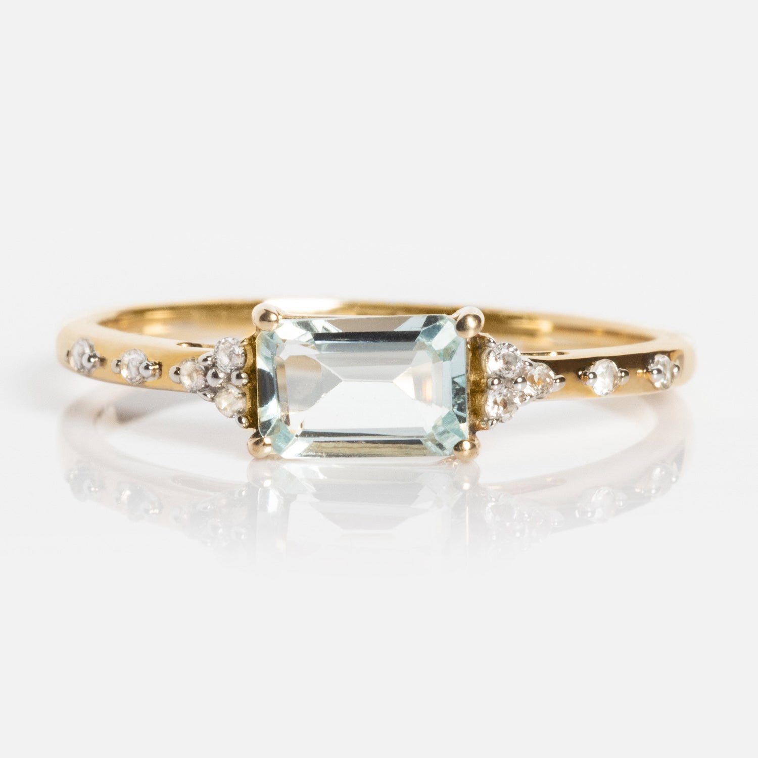 The Solid Gold Glimmering Birthstone Baguette Ring features a rectangular, emerald-cut light green gem at the center, accented by round and pear-shaped clear stones plus petite stones on the band—a Family Gold exclusive.