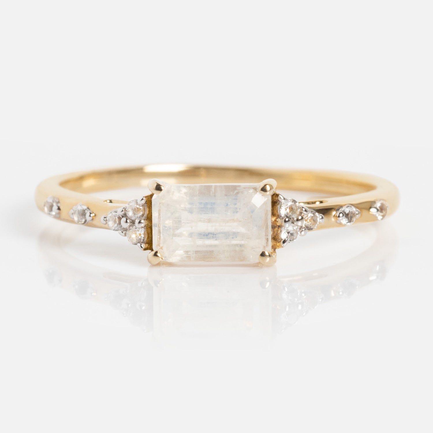 The Solid Gold Glimmering Birthstone Baguette Ring showcases a rectangular baguette gemstone center, with white topaz accents and round diamonds along the band, displayed against a white background.