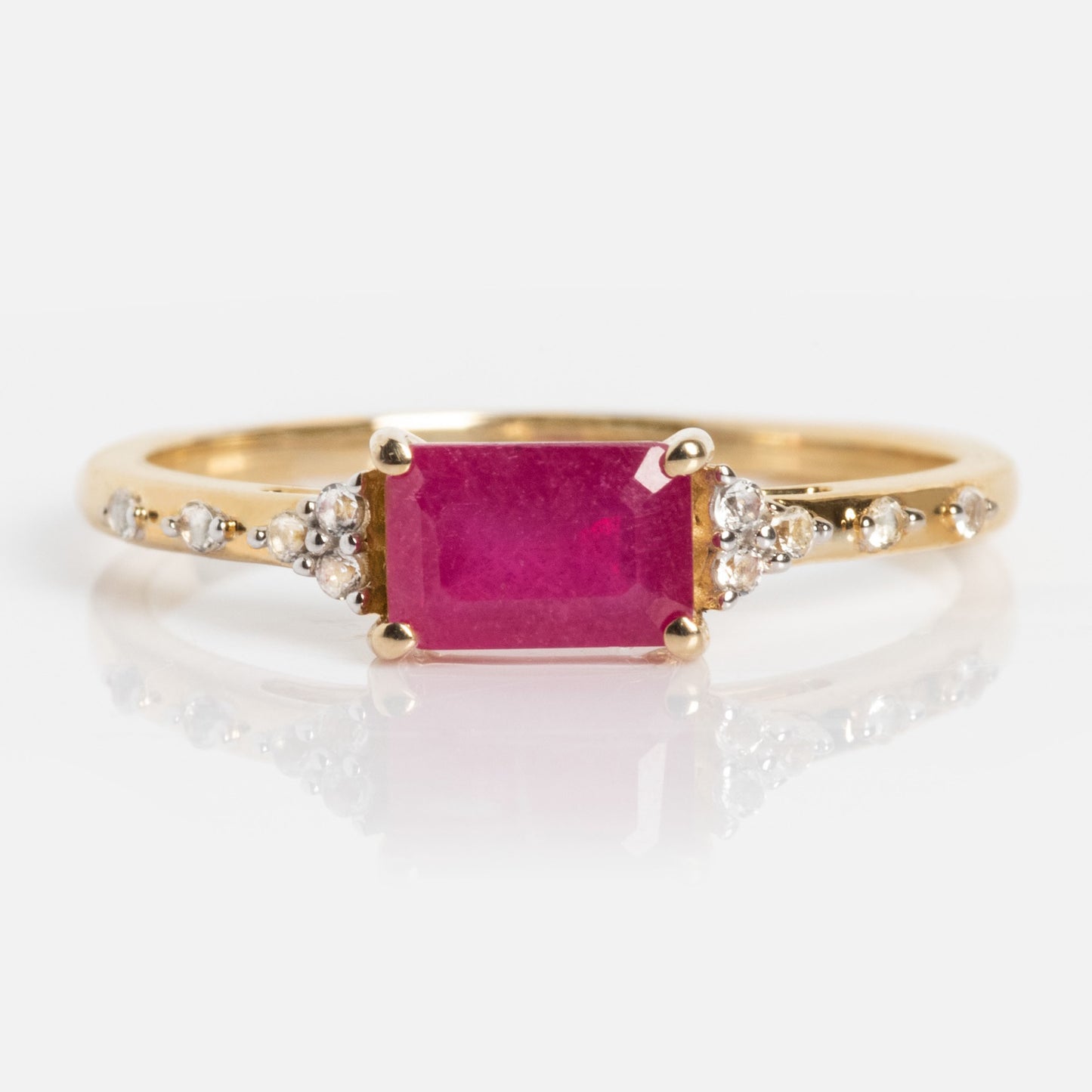 The Solid Gold Glimmering Birthstone Baguette Ring features a rectangular bright pink baguette gemstone at the center, accented by sparkling white topaz on each side, displayed against a white background.