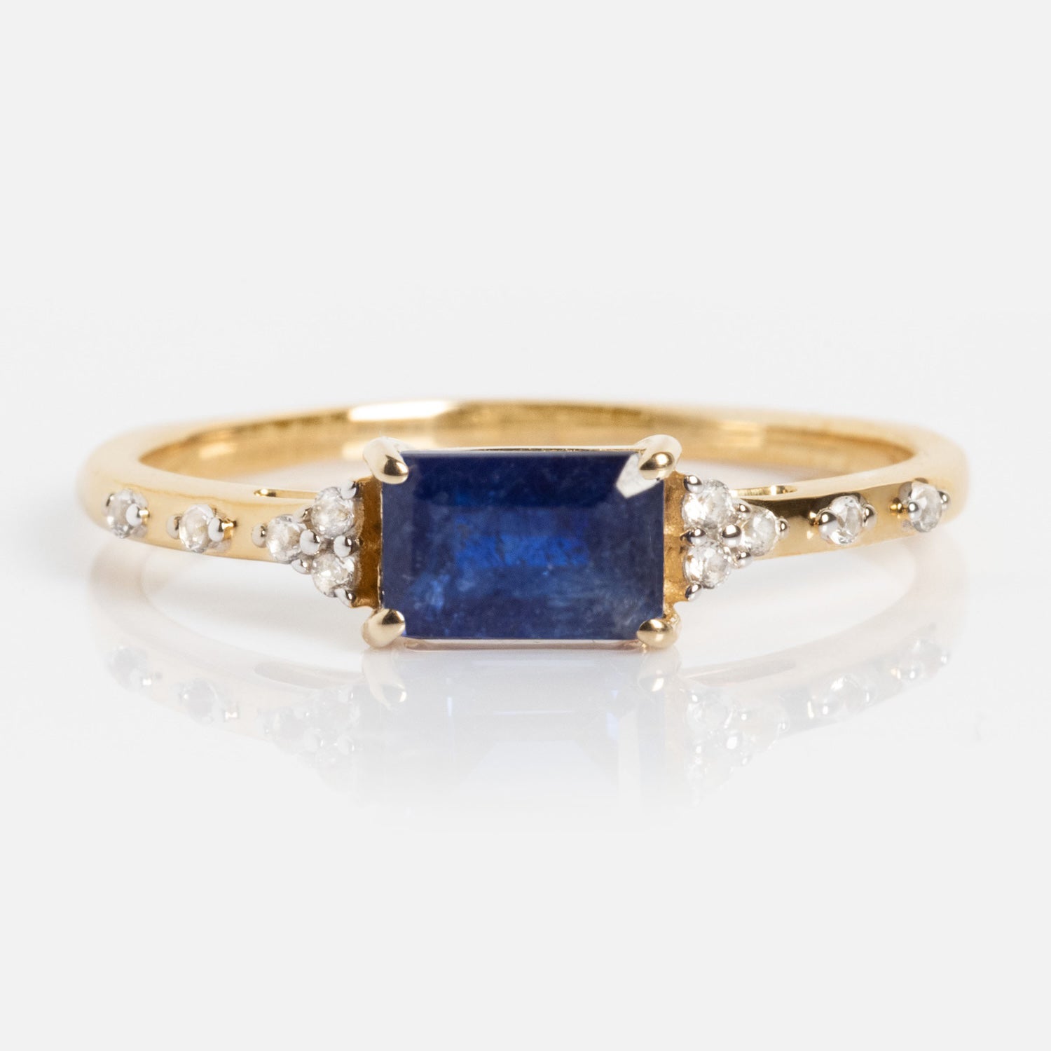 The Solid Gold Glimmering Birthstone Baguette Ring showcases a central rectangular gemstone, accented by sparkling white topaz along the band, beautifully displayed against a white background.