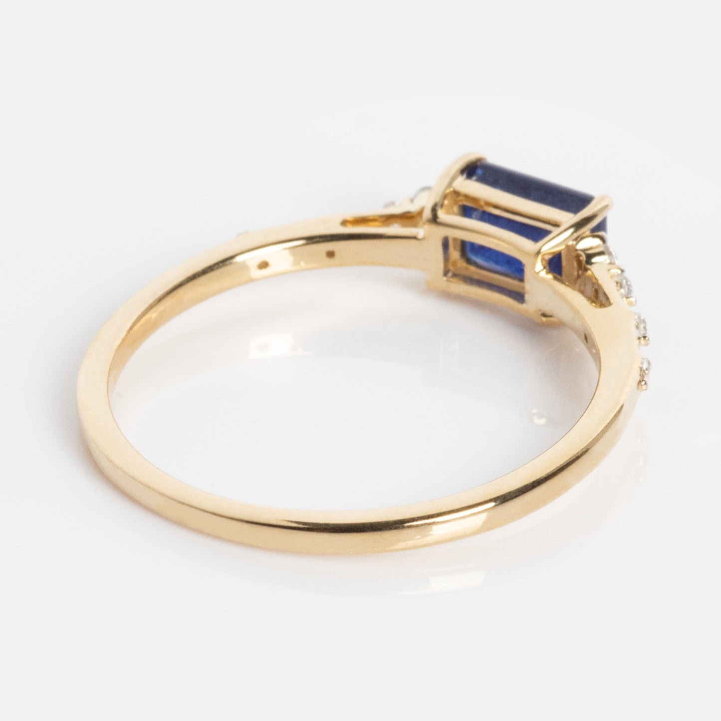 The Solid Gold Glimmering Birthstone Baguette Ring features a rectangular blue baguette gemstone in raised prongs with clear accent stones on the band, all crafted in solid gold and shown against a white background.