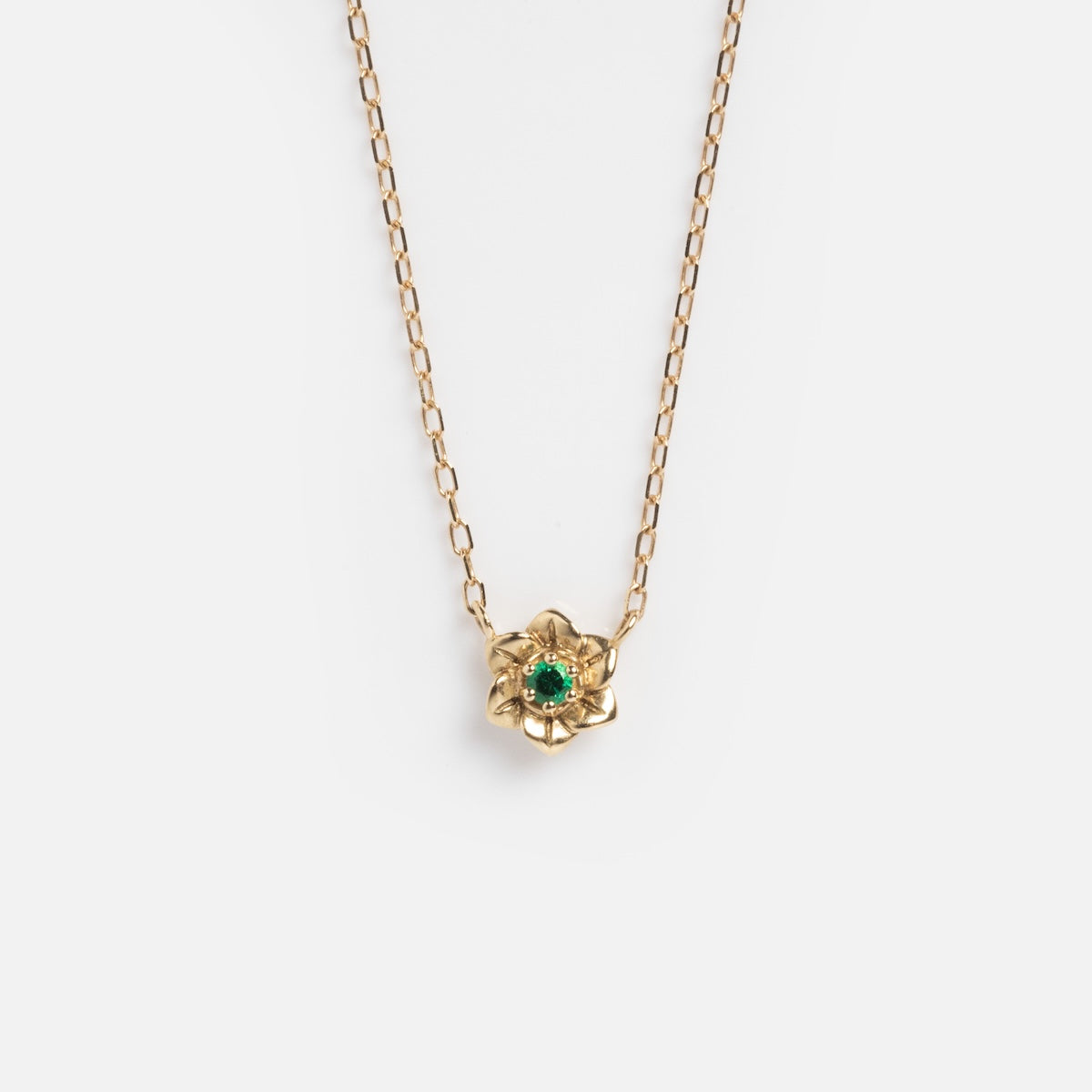 The Solid Gold Birth Flower Bloom Necklace features a delicate chain with a small, flower-shaped pendant set with a green gemstone at the center, displayed on a plain white background.