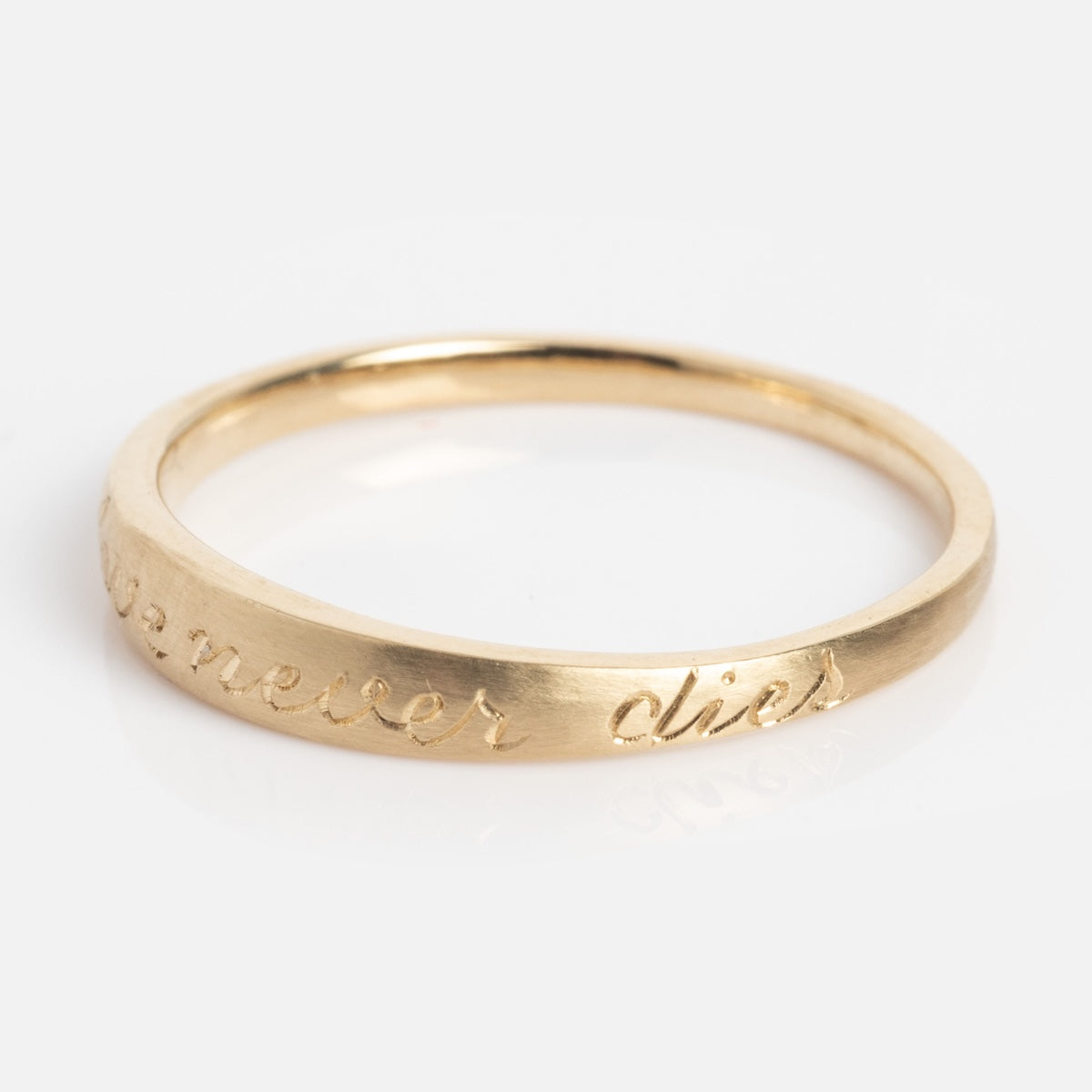 The True Love Never Dies Band is a slim gold ring featuring an engraved cursive inscription, "never dies," on its outer surface, shown against a white background.