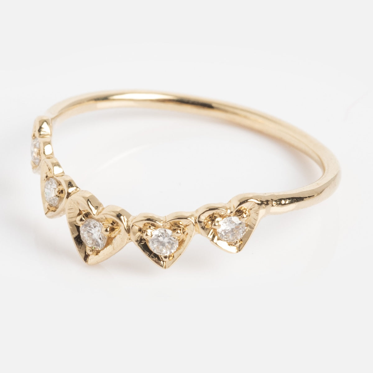 The Radiant Hearts Band (outward band) is a delicate gold ring with five heart-shaped settings, each set with a small clear gemstone, arranged in a row along the band.