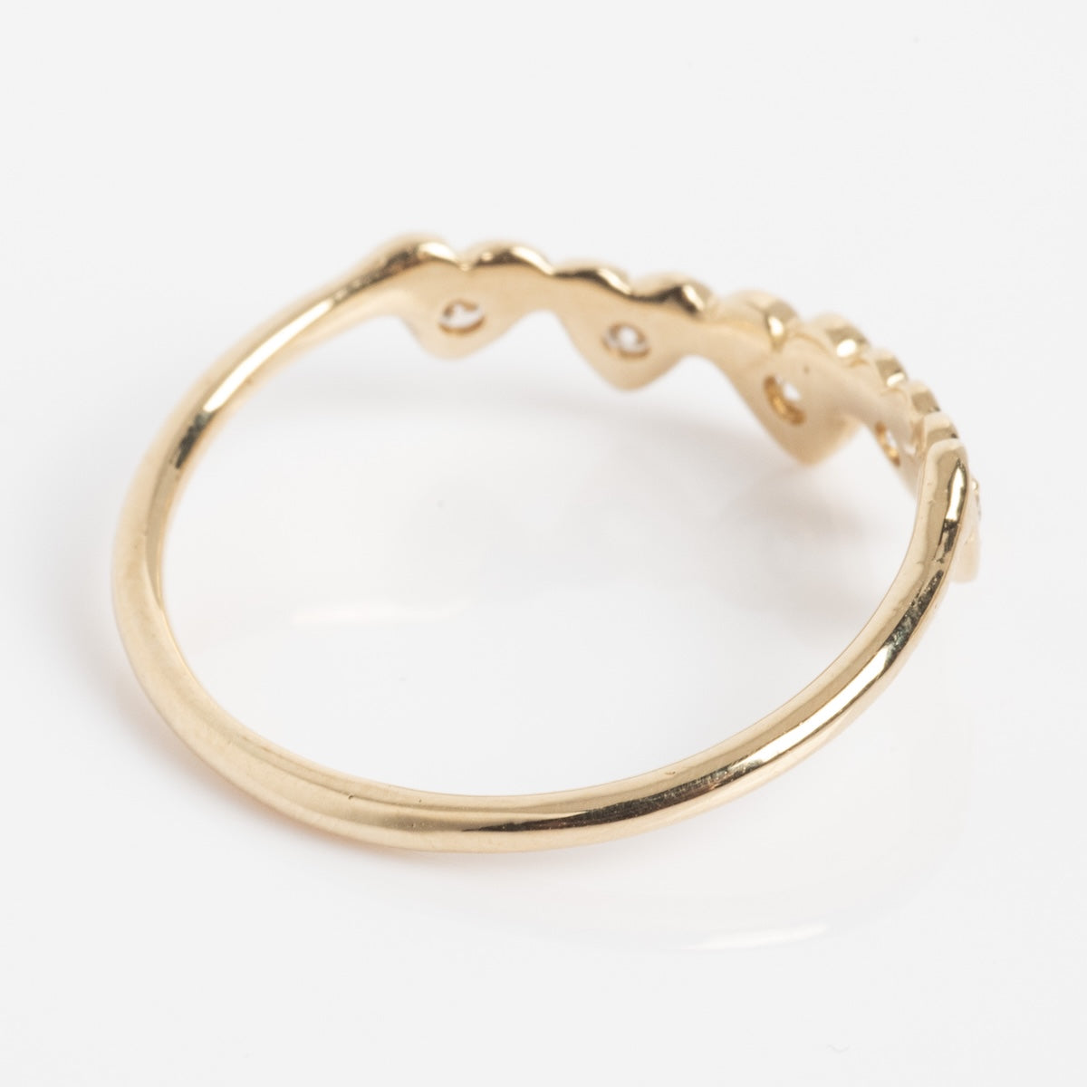 The Radiant Hearts Band (outward band) is a thin gold ring featuring a scalloped, wave-like design on top and small round cutouts along the raised edge, shown on a white background.