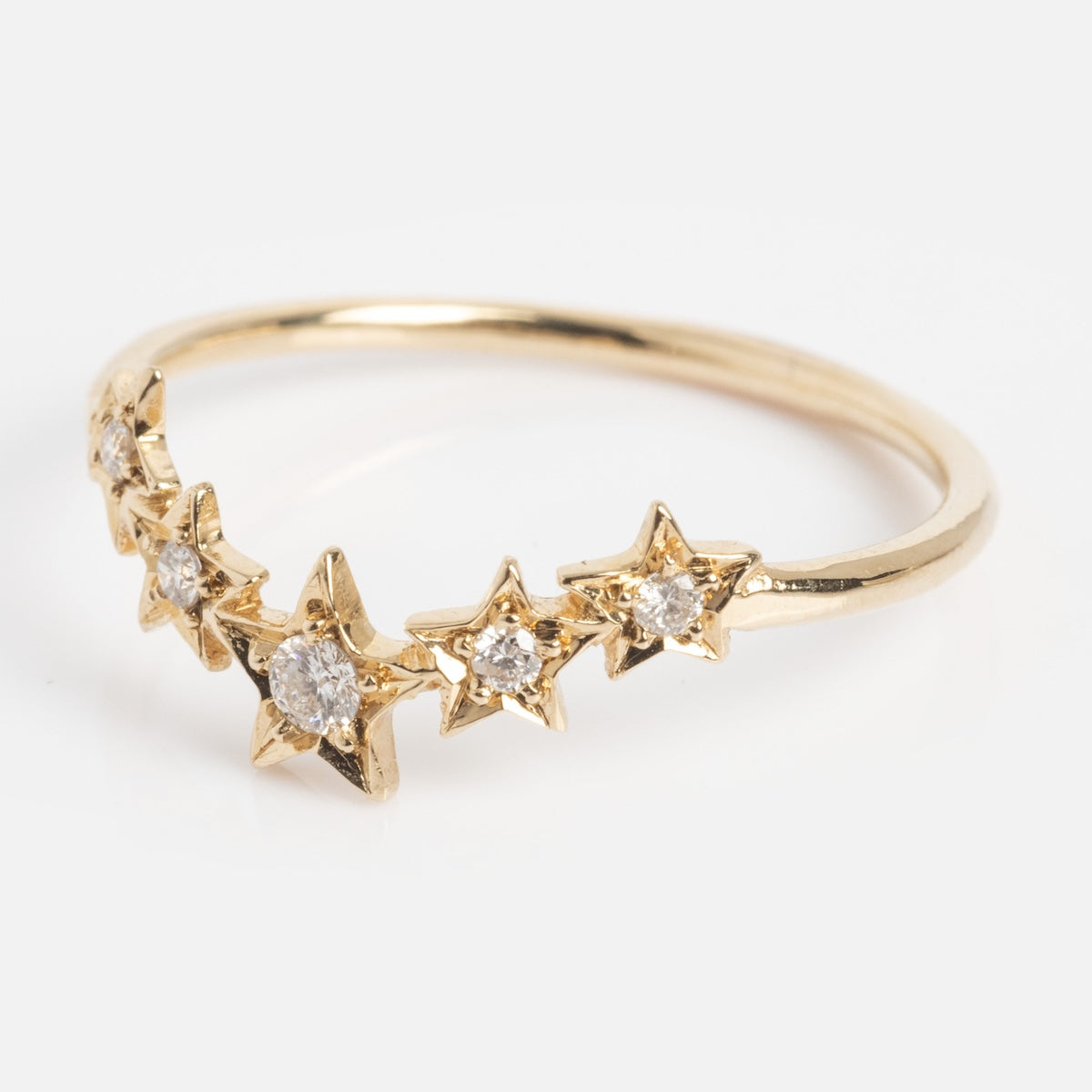 The Stars Aligned Band is a delicate gold ring with five star-shaped settings, each set with a sparkling diamond, arranged in a graceful curve.