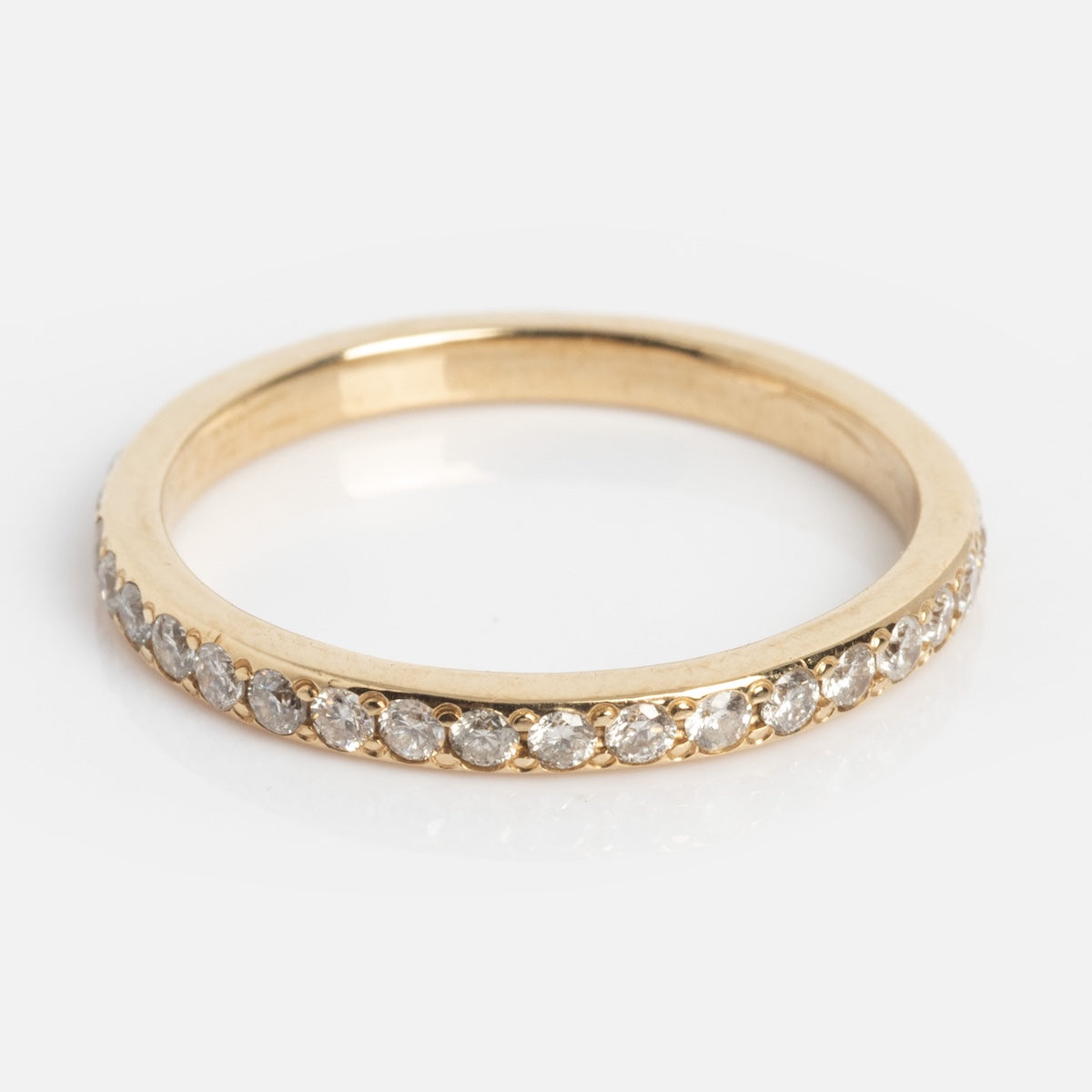 The Infinity Diamond Band features a row of small, round white diamonds set along the top half of a gold band, displayed on a white background.