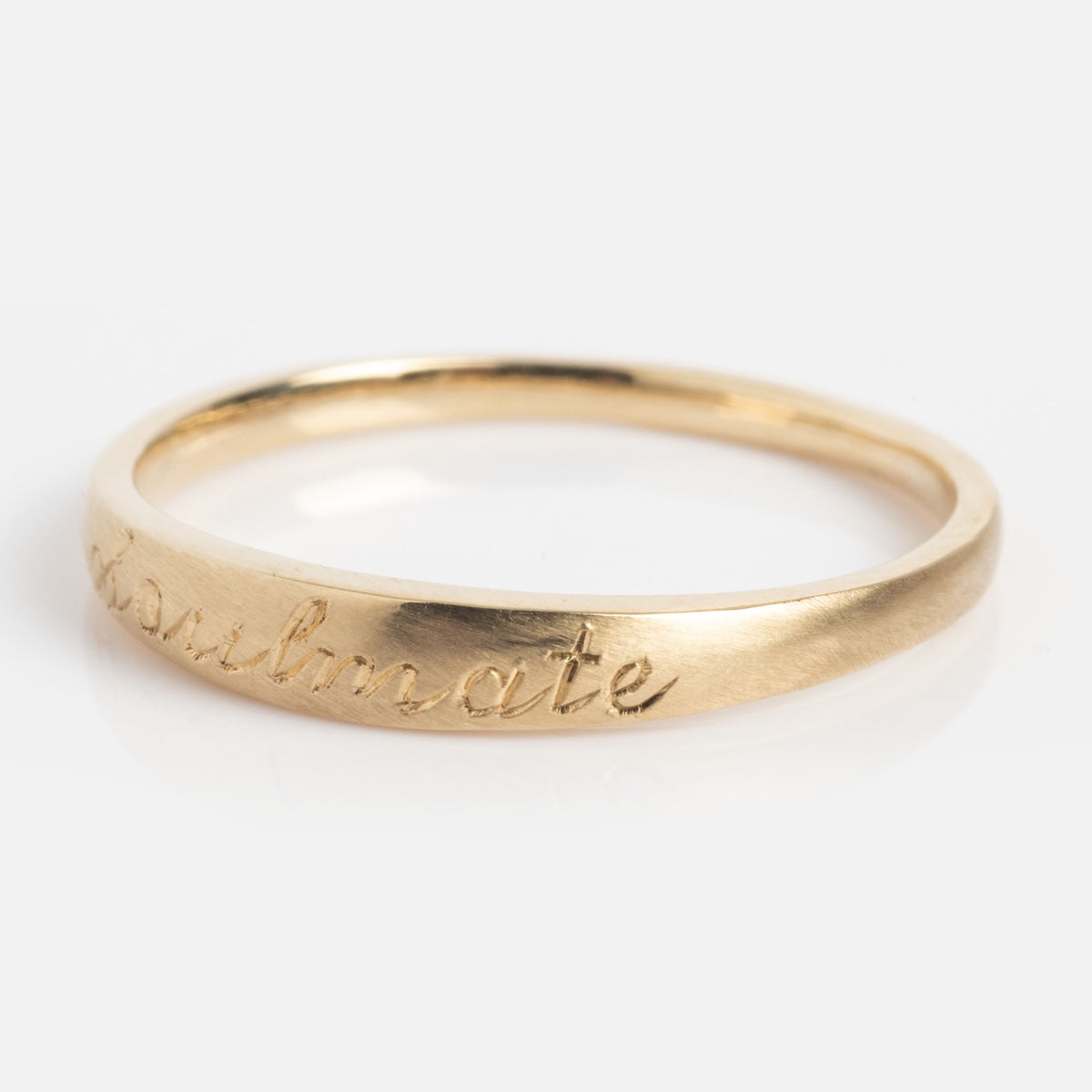 The Soulmate Band is a simple gold ring engraved with 'soulmate' in cursive on its outer surface, shown against a plain white background.