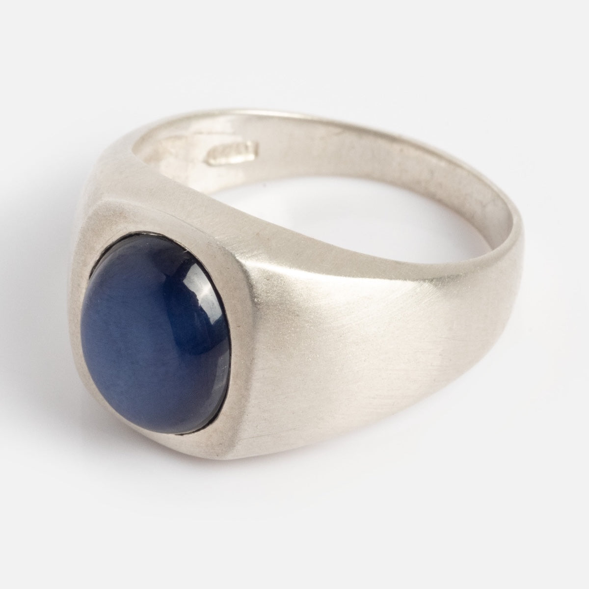 The Guardian Ring is a silver wide band ring with a smooth, round dark blue gemstone set in a bezel setting against a plain background.