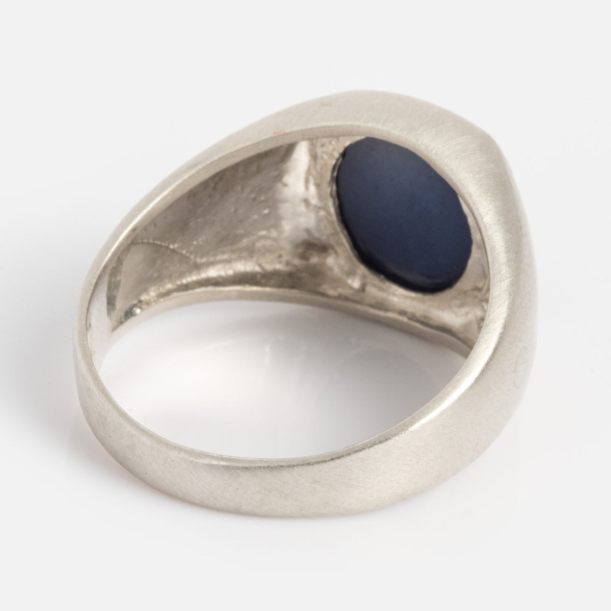 The Guardian Ring features a smooth, rounded silver band with an open-back setting showcasing a dark blue, oval-shaped stone. Displayed from the underside, the ring sits against a plain white background.