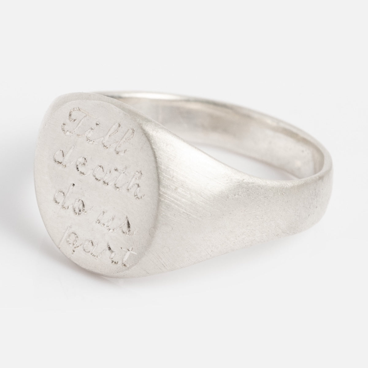 The Till Death Do Us Part Signet Ring is a silver ring featuring an engraved inscription on its oval face that reads "till death do us part" in a delicate, handwritten style.