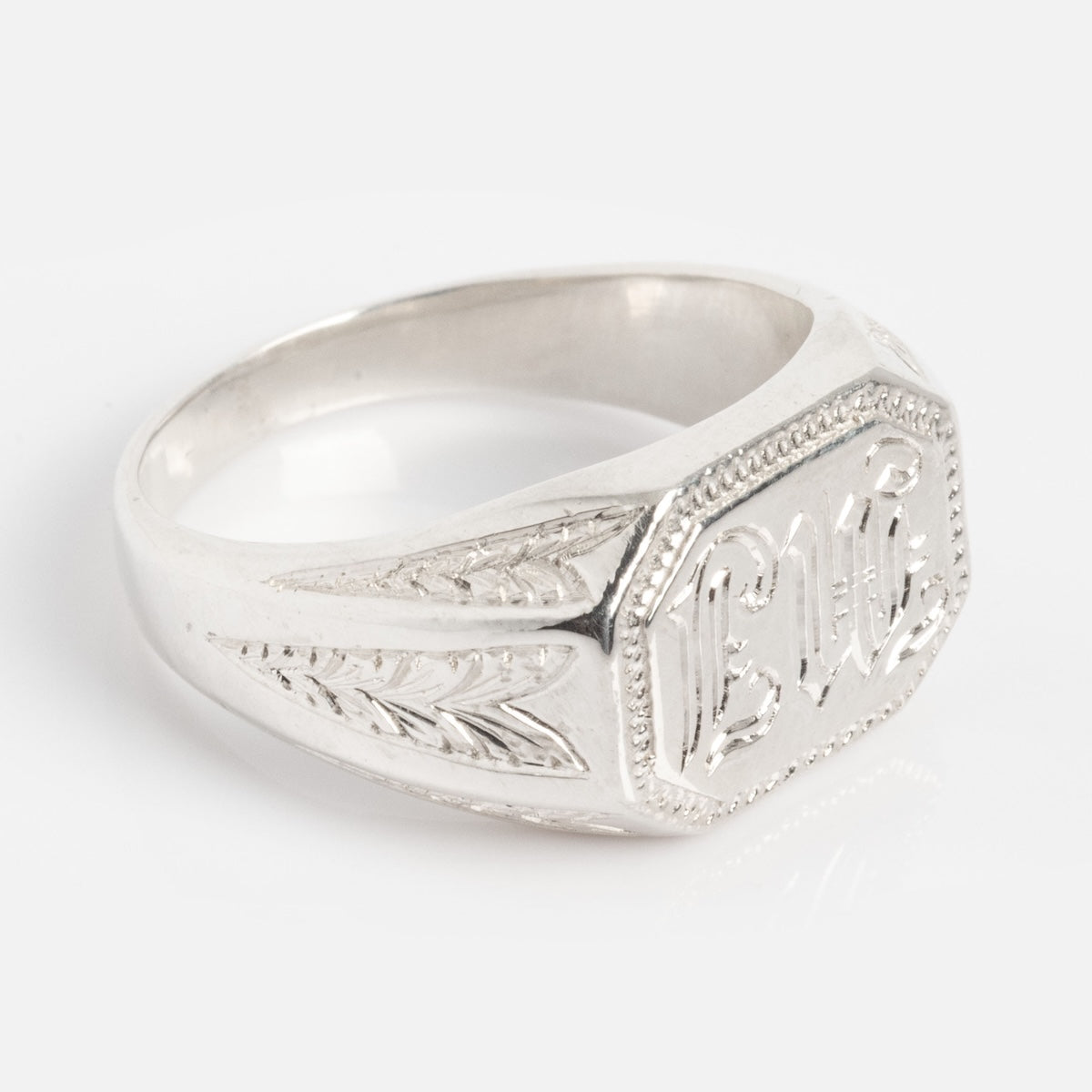 The Sovereign Signet Ring features an engraved script on its flat, octagonal silver face with decorative leaf patterns on the sides, displayed against a plain white background.