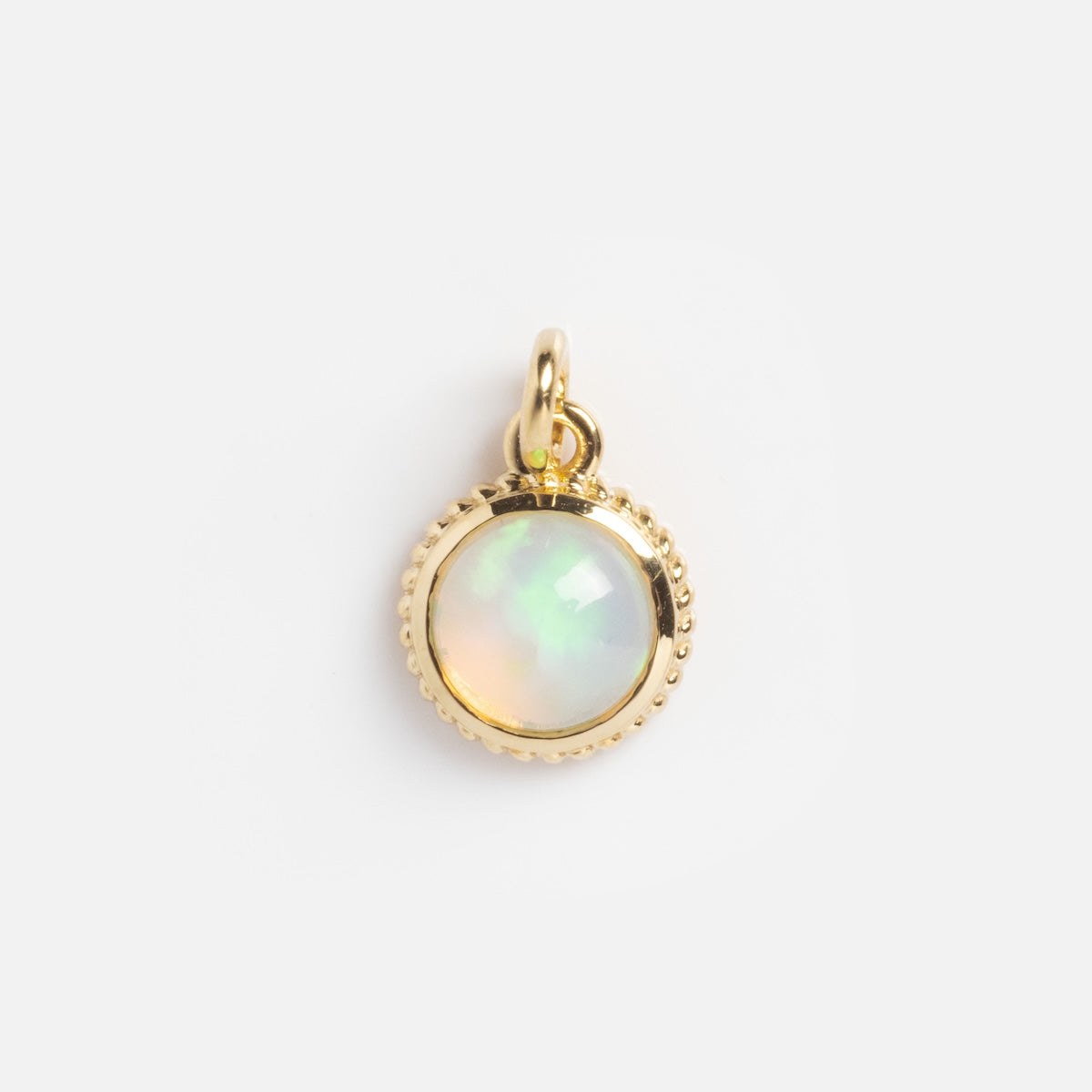 The Solid Gold Statement Charm is a small, round pendant with a beaded edge and an iridescent opal center, displayed on a plain white background.