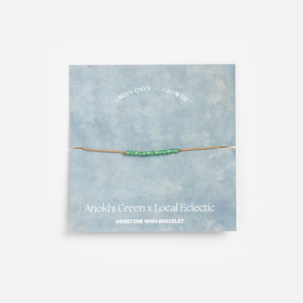 The Anokhi Green x Local Eclectic Gemstone Wish Bracelet features small green onyx beads on a thin gold chain, displayed on a blue card and crafted with natural gemstones for growth.
