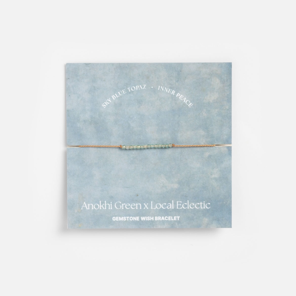 A delicate intention bracelet with natural sky blue topaz gemstones on a thin cord, shown on a blue card labeled Anokhi Green x Local Eclectic Gemstone Wish Bracelet – Sky Blue Topaz Inner Peace.