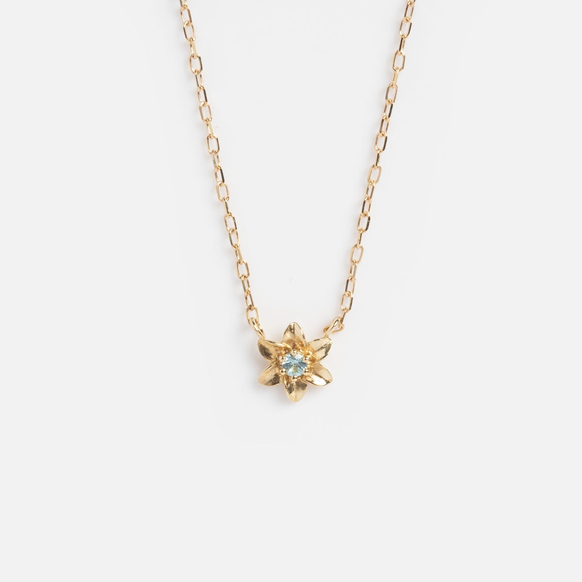 Solid Gold Birth Flower Bloom Necklace featuring a delicate chain and a small, flower-shaped pendant with a central gemstone, displayed on a plain white background.