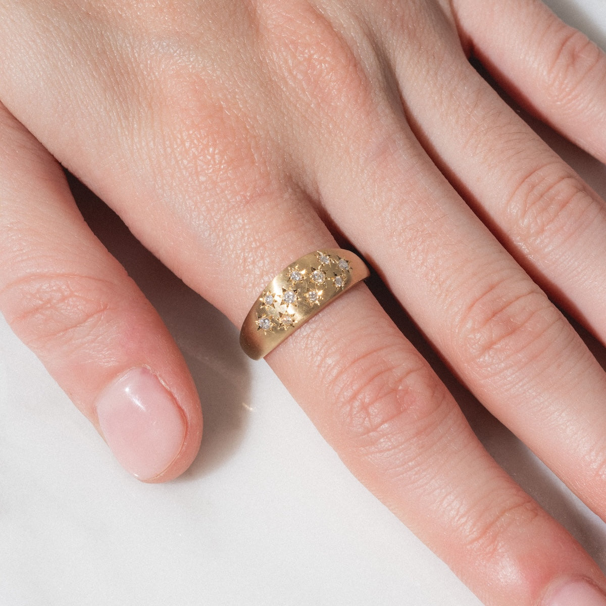 A close-up of a hand wearing the Half Moon Bombe Ring—a wide gold band with engraved star patterns—on the middle finger, set against a light background.