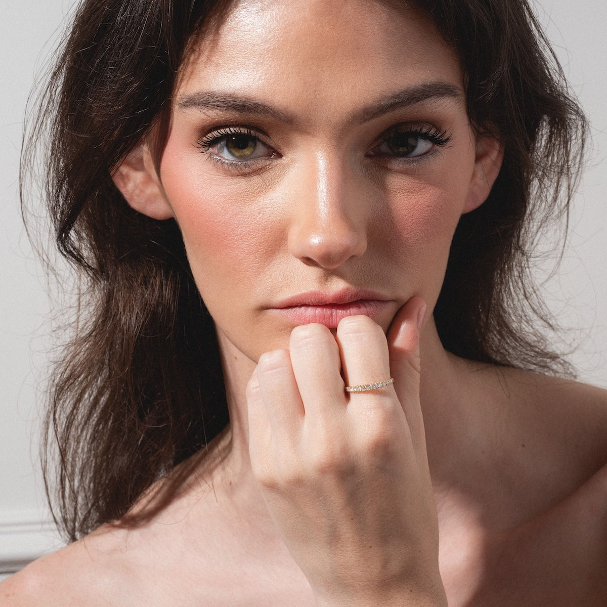 A woman with long brown hair and natural makeup poses with her hand on her chin, showcasing the Echo Diamond Band on her finger. She has a neutral expression and is photographed against a plain background.