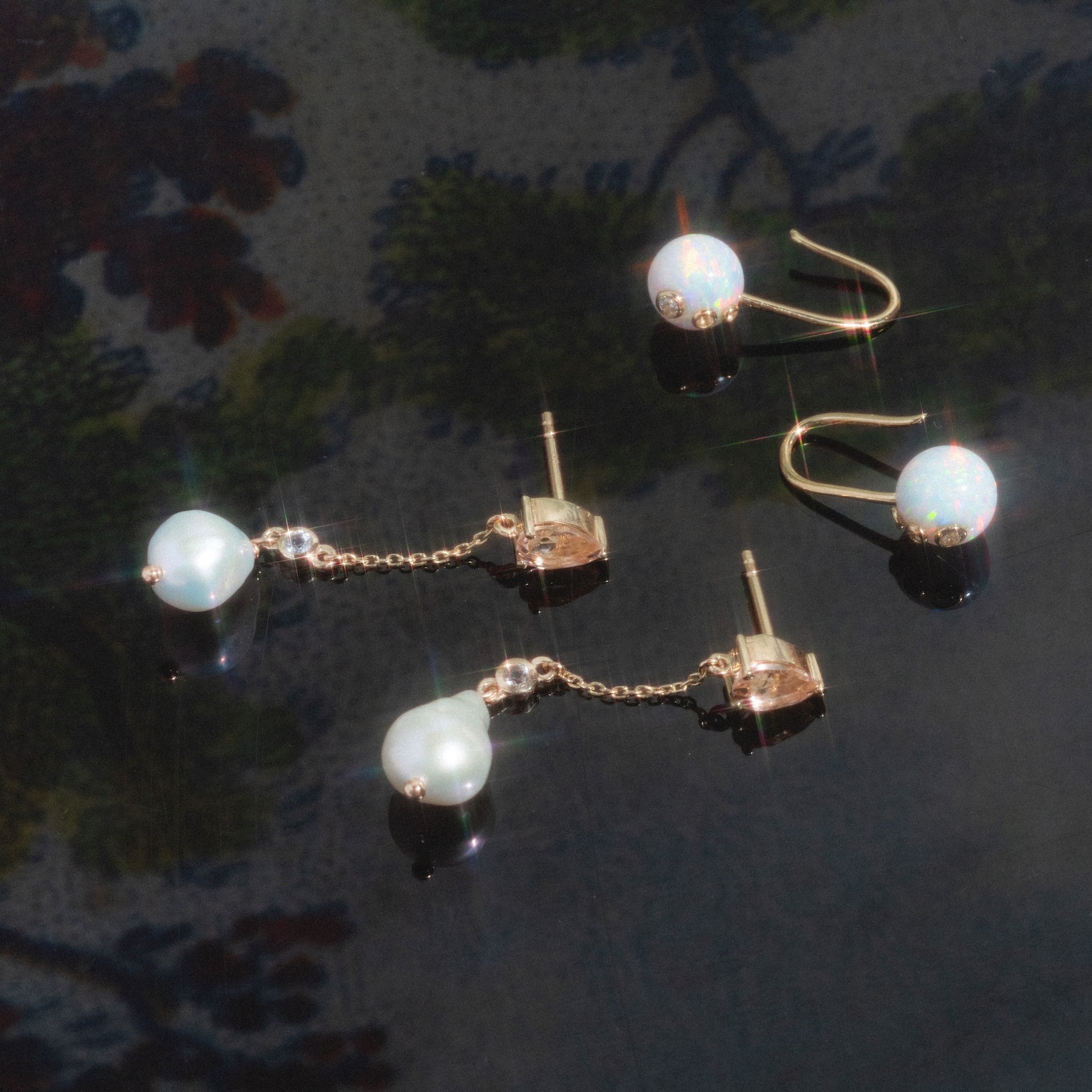 A pair of Solid Gold Citrine and Pearl Droplet Earrings displayed on a reflective dark surface with a blurred floral background.