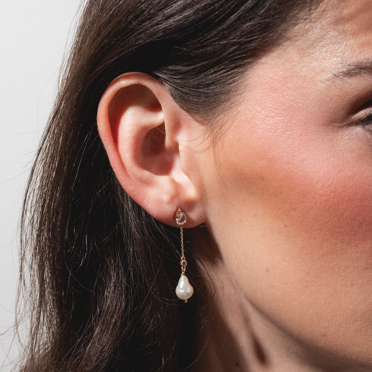 Close-up of a woman's ear wearing Solid Gold Citrine and Pearl Droplet Earrings, featuring a teardrop-shaped citrine stud and a hanging pearl. Her brown hair is tucked behind her ear, highlighting her warm, natural-toned skin.