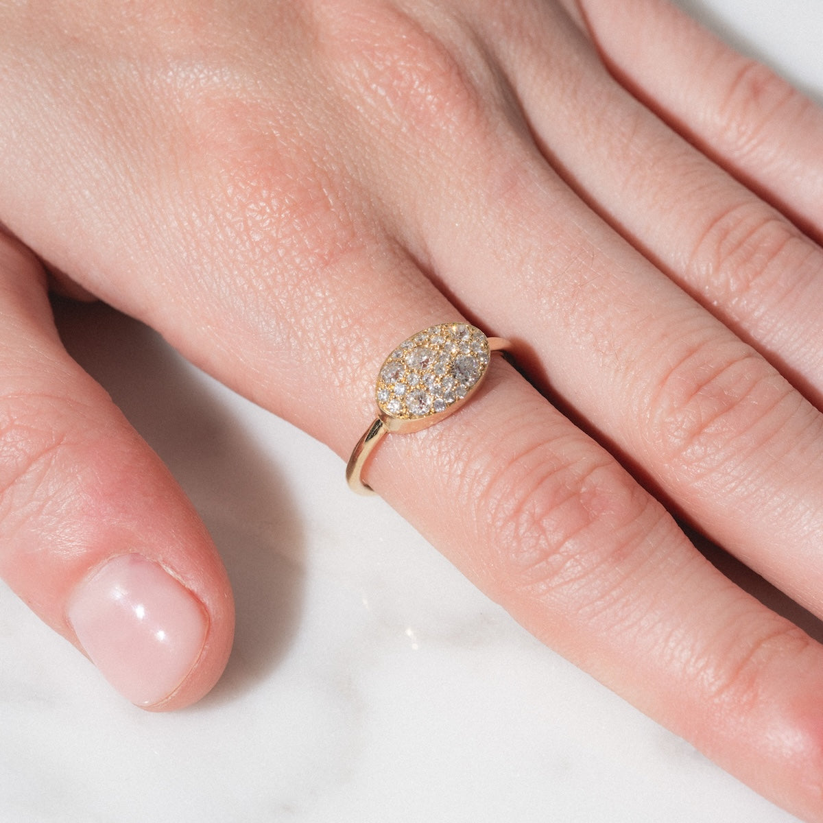 A hand rests on a white surface, wearing the "Eternal Flame" Soul Ring—a gold ring with an oval cluster of sparkling diamonds on the ring finger.