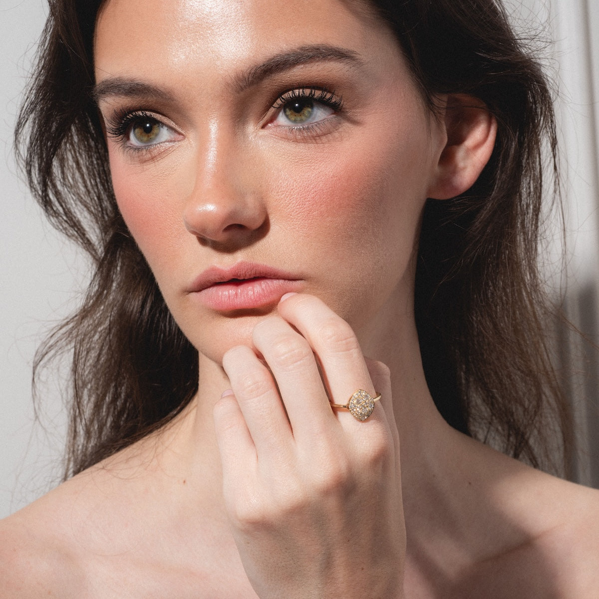 A woman with long brown hair and natural makeup gazes thoughtfully to the side, her hand near her chin, showcasing the "My Beloved" Soul Ring—a gold ring with a round, sparkling setting.