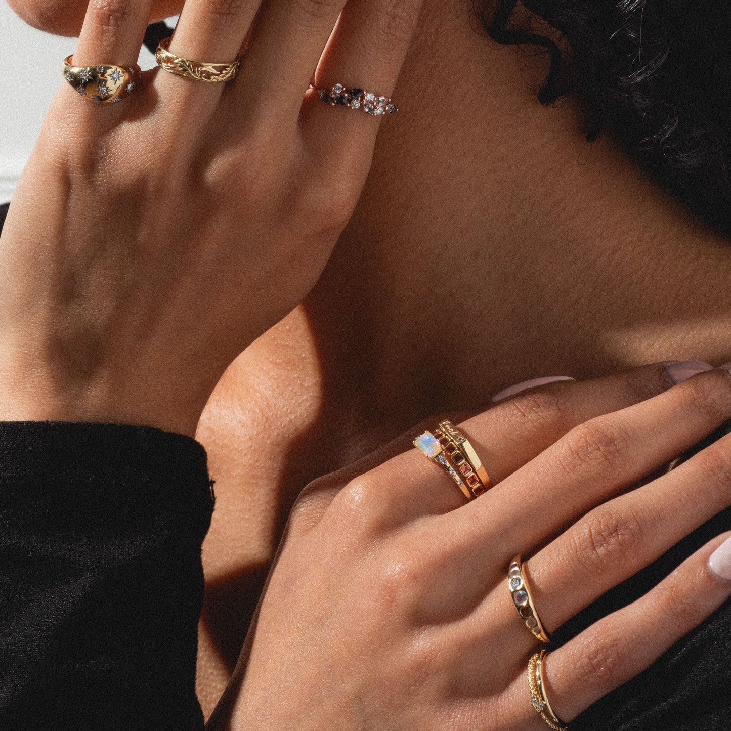 Close-up of two hands wearing the Solid Gold Star Crossed Dome Pinky Ring, with star set diamonds, shown against bare skin and a black sleeve. Lighting highlights the ring's intricate details.