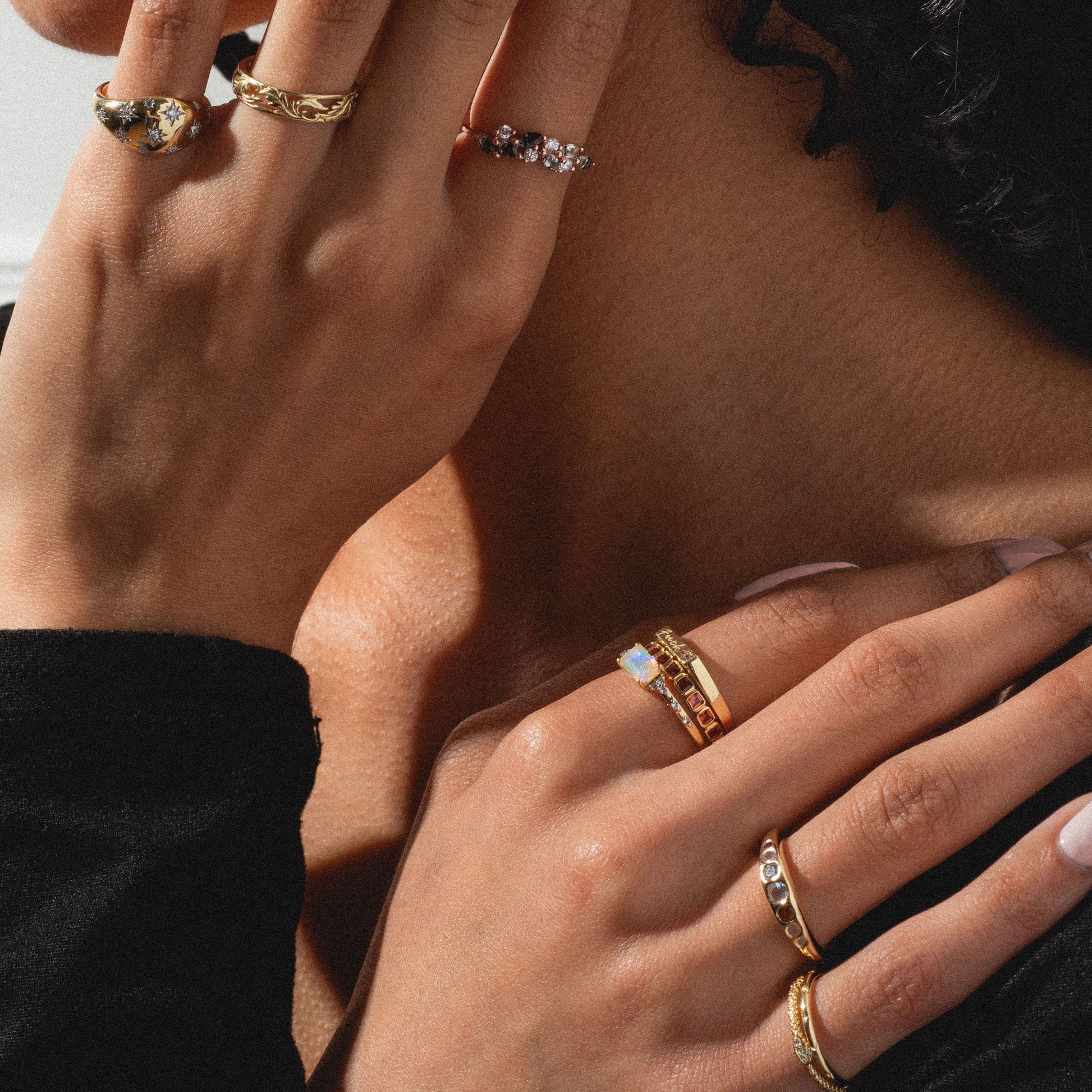 Close-up of two hands wearing the Solid Gold Star Crossed Dome Pinky Ring, with star set diamonds, shown against bare skin and a black sleeve. Lighting highlights the ring's intricate details.