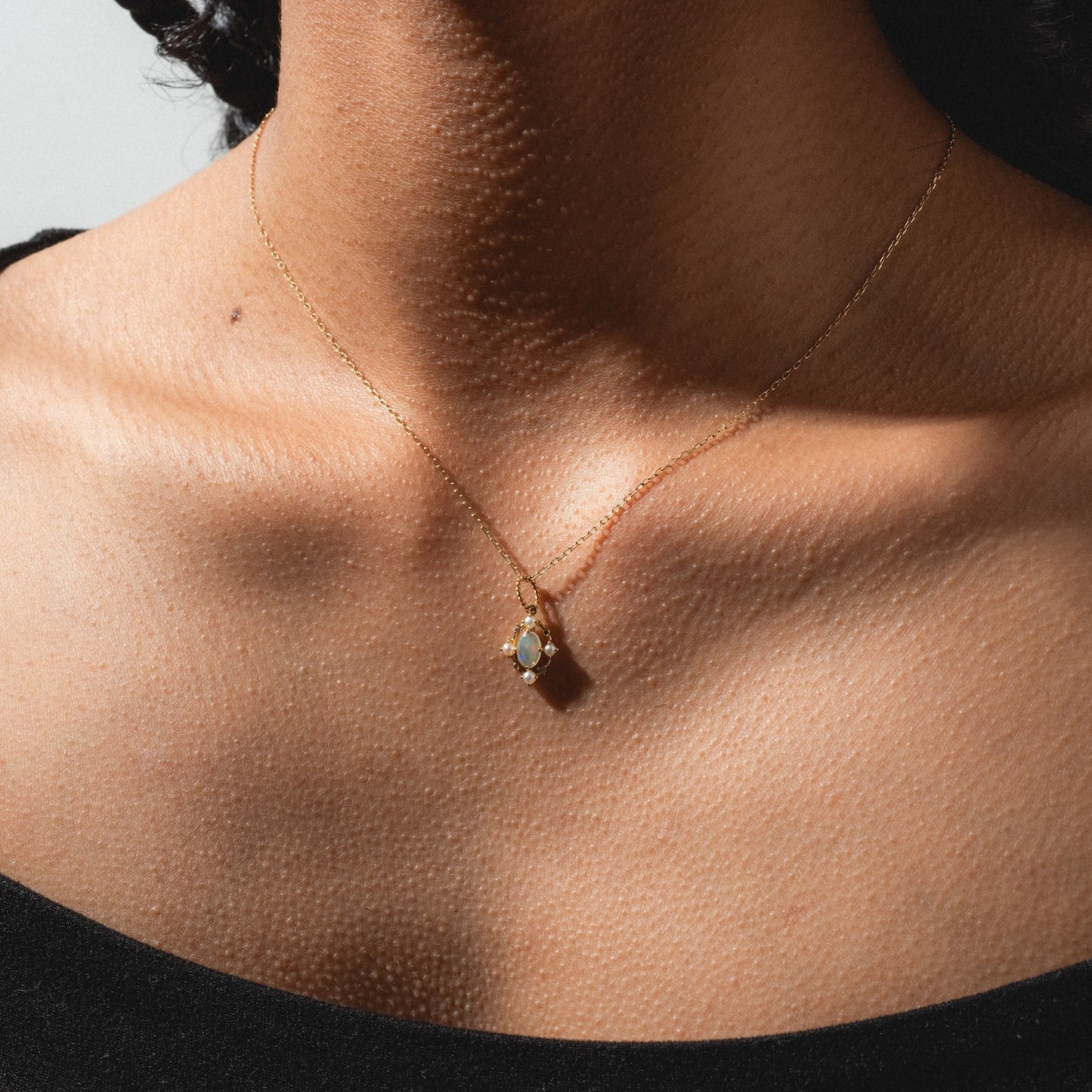 A person’s neck and collarbone are shown wearing the Solid Gold 2025 October Capsule Opal Statement Set—a delicate gold chain with an opal pendant—against a plain background, paired with a black top. Comes with a free gift.