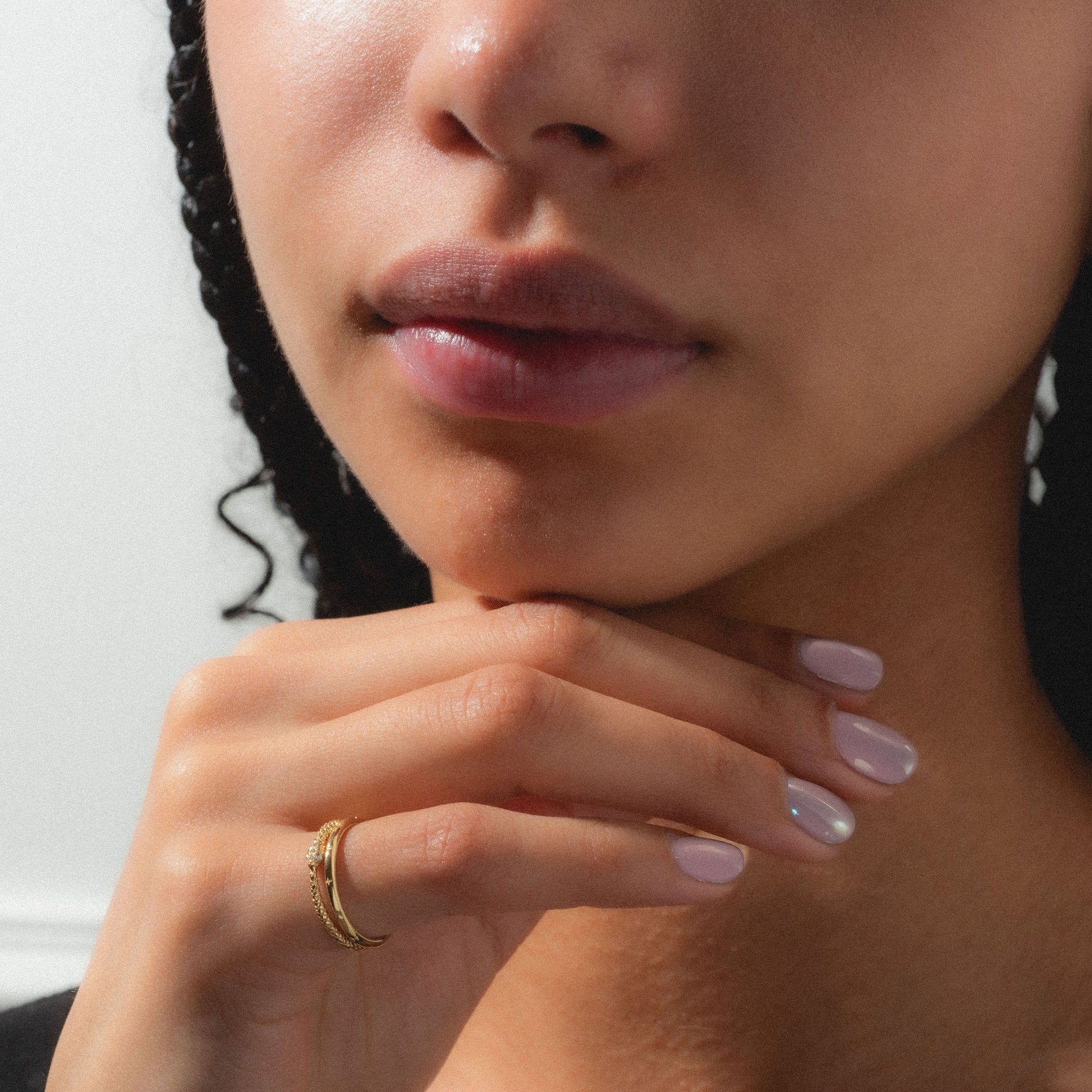 A close-up shows a person with natural lips and clear skin, resting their chin on manicured fingers adorned with a light polish and wearing the Ouroboros Diamond Snake Ring.