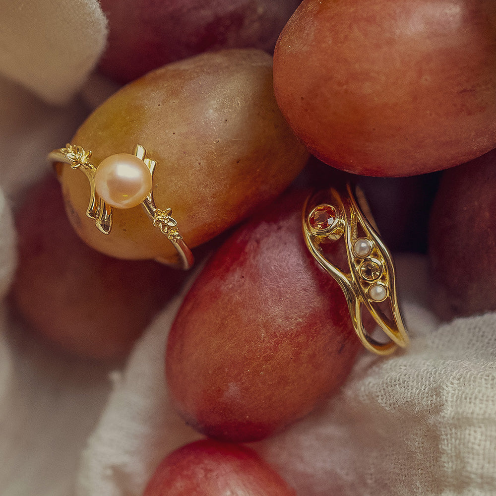 The 10k Orange Sapphire and Citrine Bayside Ring is displayed on a cluster of red grapes, partially surrounded by a white cloth.