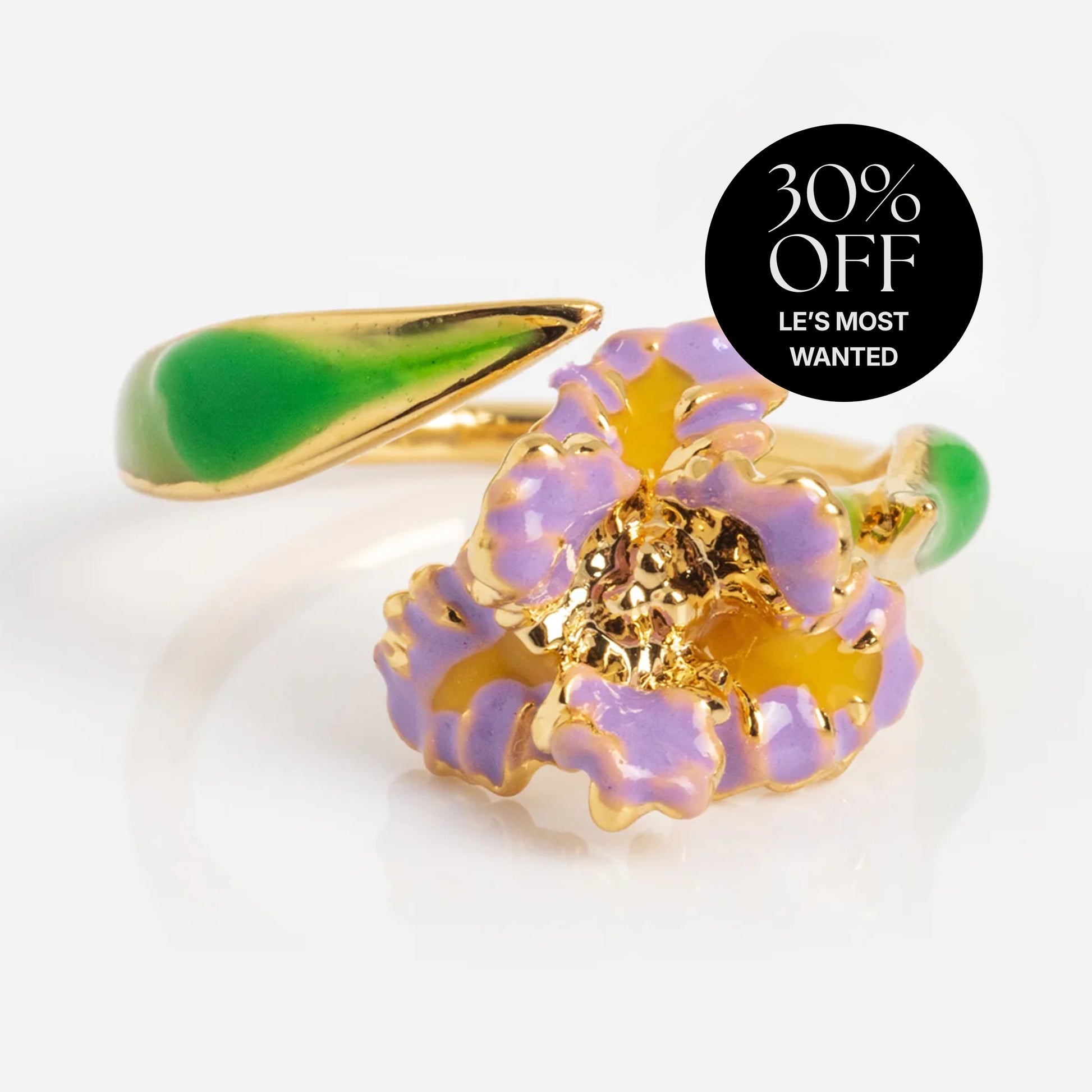The Blooming Color Adjustable Enamel Birth Flower Ring February Sample is a 14k yellow gold plated ring with a green enamel band, featuring a purple and yellow flower design and a “30% OFF LES MOST WANTED” label.