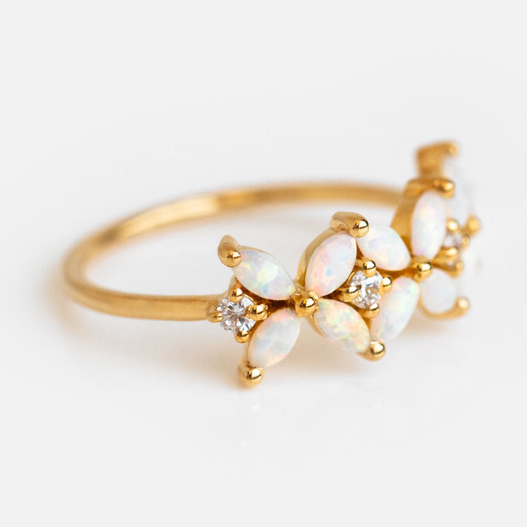 The Opal Fae Ring is a delicate yellow gold floral ring with marquise-shaped opal petals and small round diamonds between them, set against a white background.