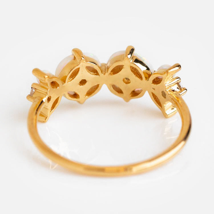 The Opal Fae Ring is a yellow gold ring with an intricate side setting holding three gemstones. Its floral design features a shiny finish and delicate, elegant details, shown against a white background.