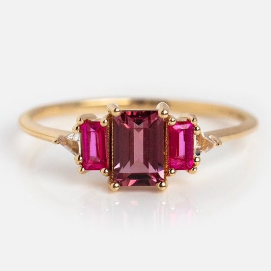 The 14kt Gold Rhodolite Garnet and Topaz Cascading Love Ring (Sample Size 7) features a rectangular pink topaz center, flanked by two smaller rectangular pink stones and pairs of tiny clear accents on each side.