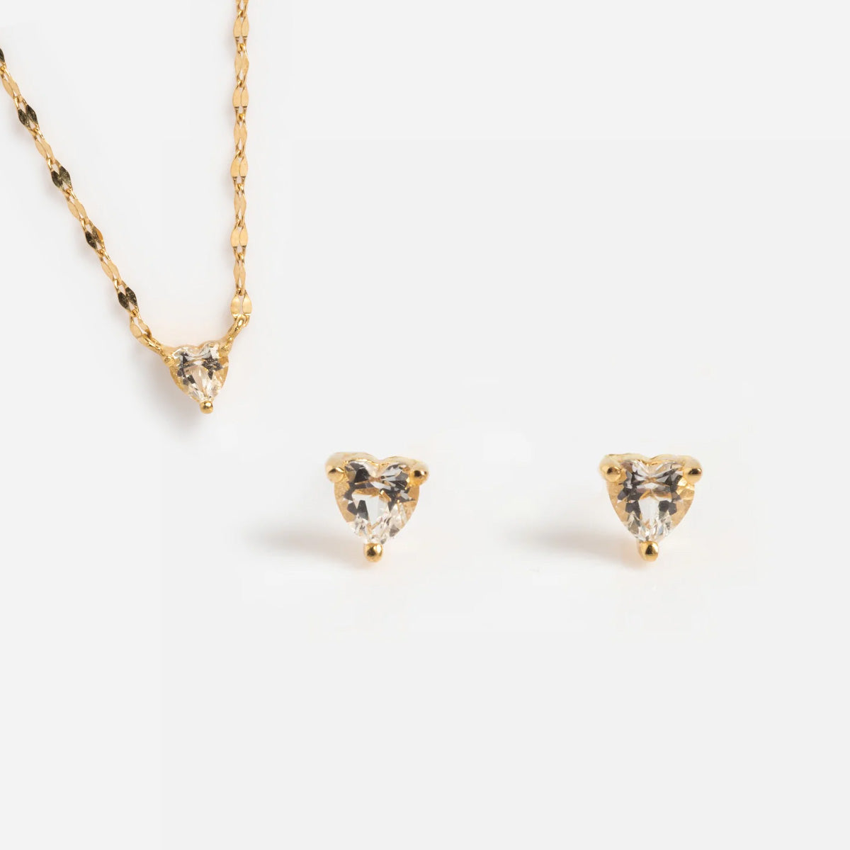 The Valentine’s Day Solid Gold Hearts Gift Set Sample features a 9k yellow gold necklace with a heart-shaped clear gemstone pendant and matching stud earrings, all displayed on a plain white background.