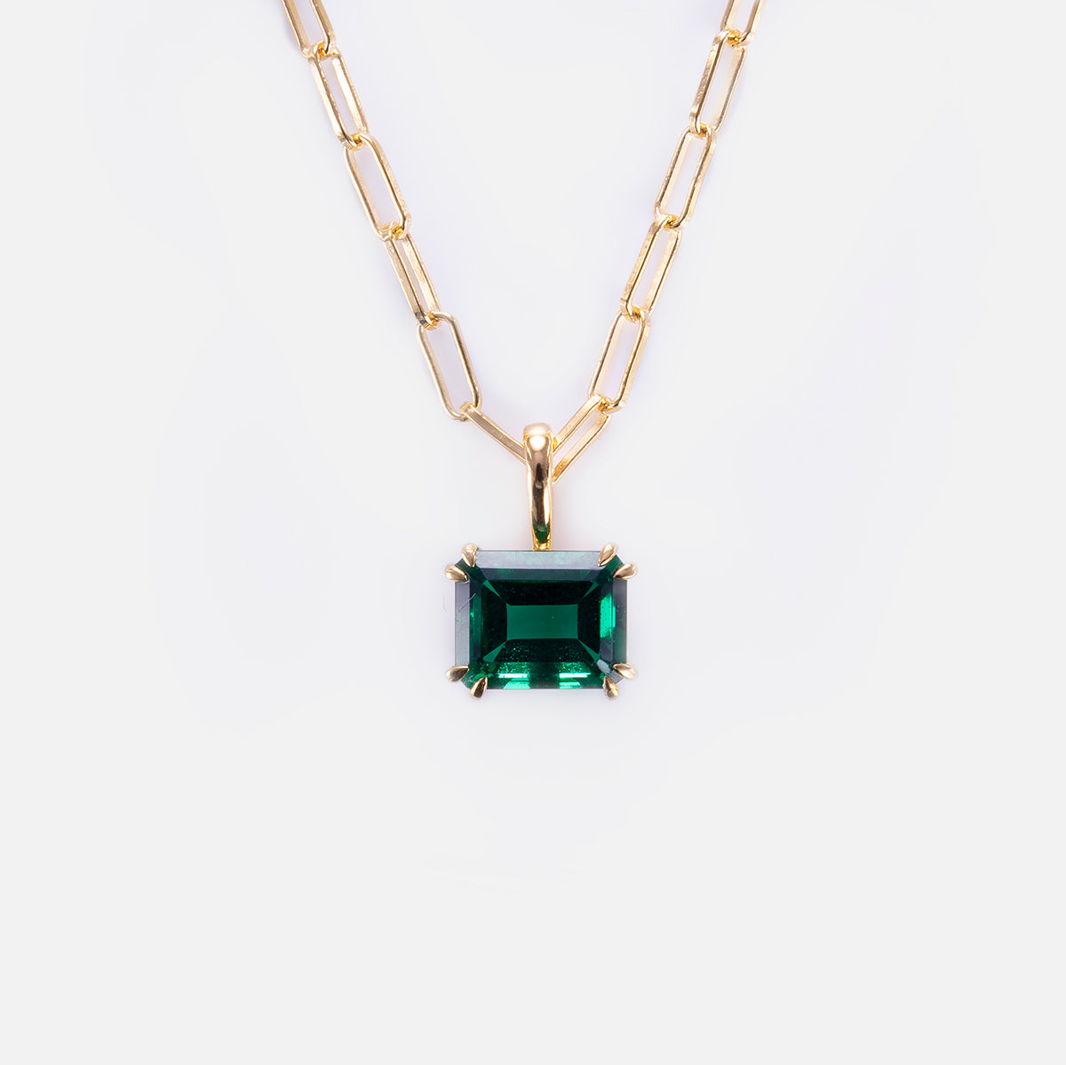 The Born to Shine Birthstone Necklace features a gold paperclip chain with rectangular links and a large emerald-cut green gemstone pendant in a gold prong setting, shown against a plain white background.