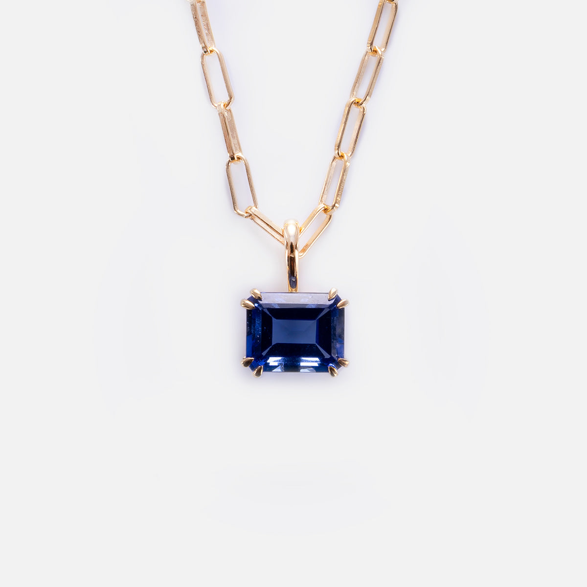 The Born to Shine Birthstone Necklace features a gold paperclip chain with a rectangular, deep blue gemstone pendant in a gold prong setting, displayed on a plain white background.