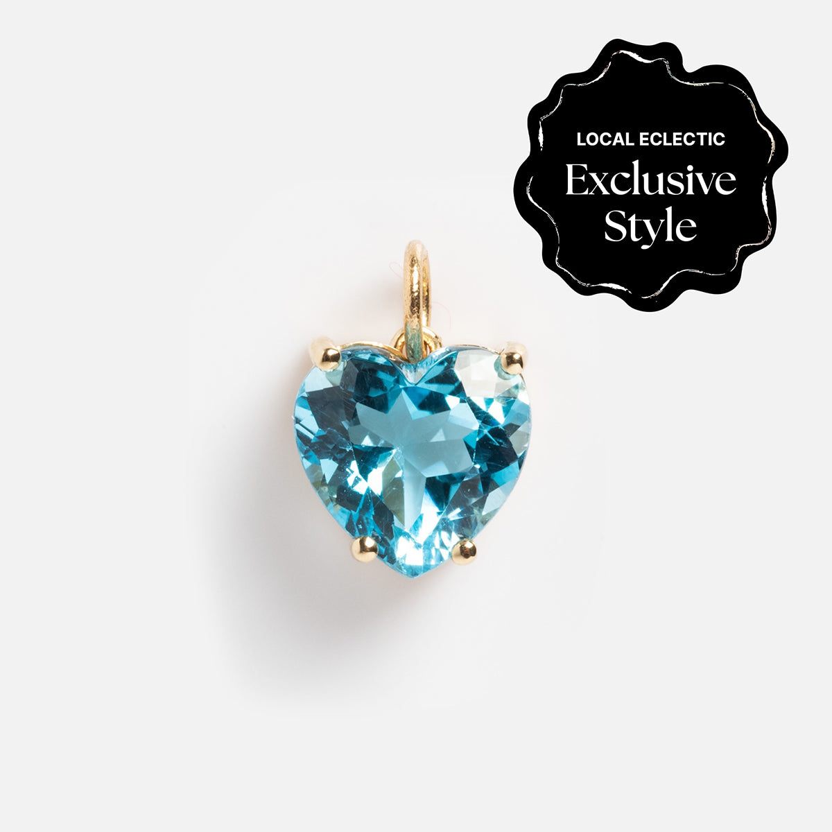 The One of a Kind 14k Blue Topaz Heart Charm features a heart-shaped blue topaz in a simple prong setting with a gold loop. A black label in the corner reads Local Eclectic Exclusive Style. White background.