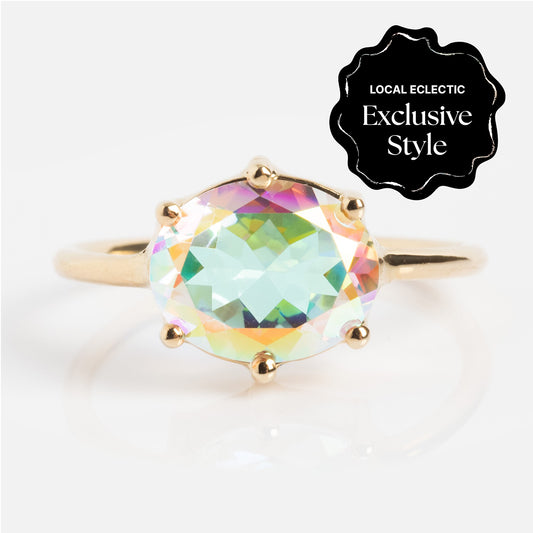 The One of a Kind 14k East West Angel Aura Ring features a large, oval, iridescent gemstone with multiple facets. A black label in the corner reads, Local Eclectic Exclusive Style.