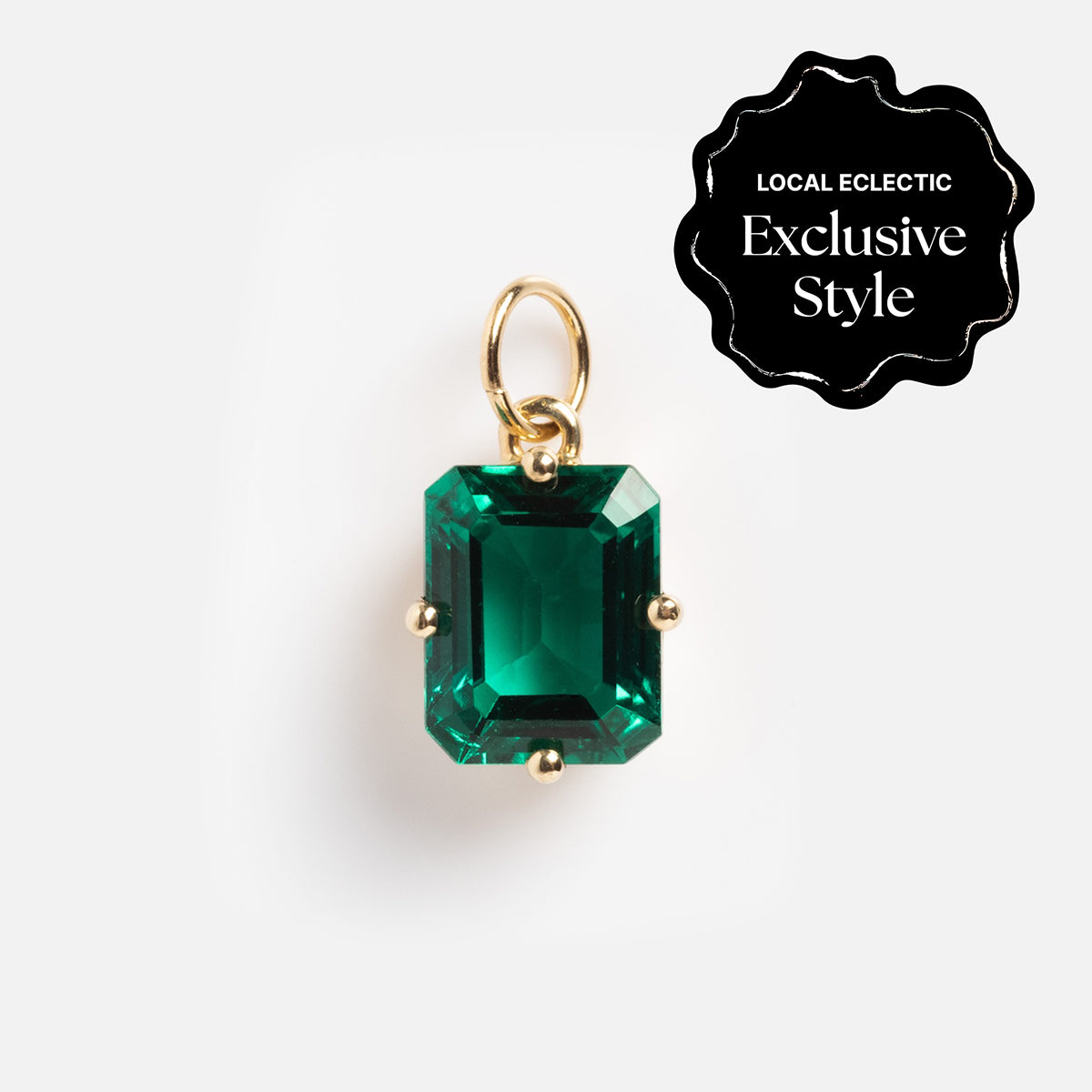 A One of a Kind 14k gold charm with an emerald-cut lab-created green gemstone and hand engraved details, shown on a white background. A black label in the corner reads Local Eclectic Exclusive Style.