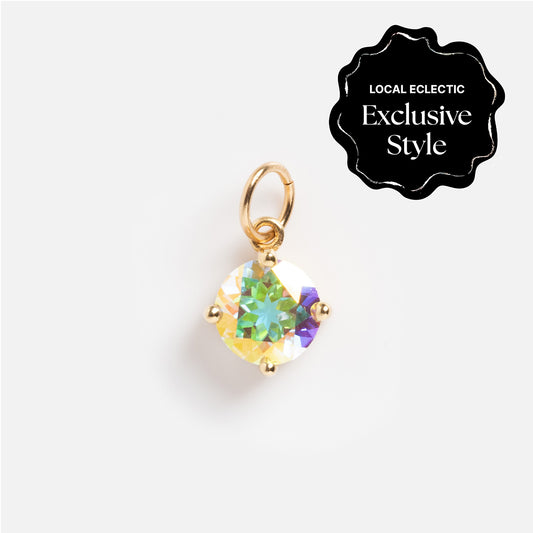 The One of a Kind 14k Round Angel Aura Charm features a round, iridescent gemstone held by four gold prongs with a small gold loop on top. A black label in the corner reads “Local Eclectic Exclusive Style.”.