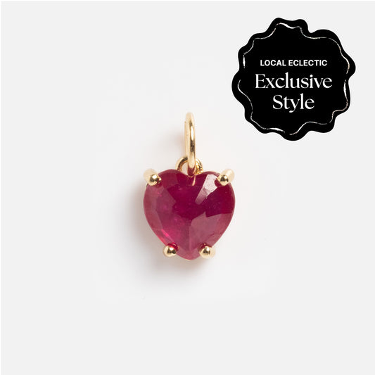 The One of a Kind 14k Ruby Heart Charm, a gold pendant with a heart-shaped red gemstone, is displayed on a white background. A black badge in the corner reads Local Eclectic Exclusive Style.